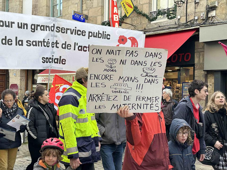 Une manifestation. Une personne tient une pancarte : « on naît pas dans les roses ni dans les choux, encore moins dans les voitures. Arrêtez de fermer les maternités »