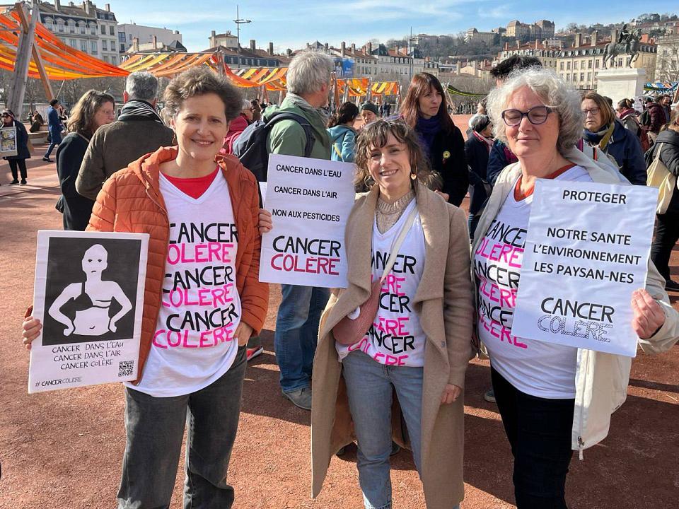 Des panneaux "Cancer colère" tenus par trois personnes