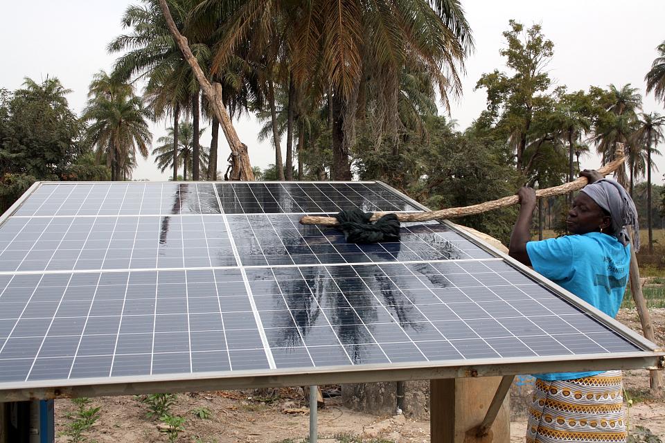 Une femme nettoie des panneaux solaires dans un jardin. 
