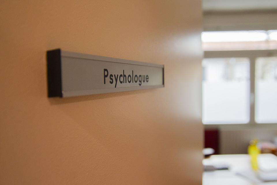 Une porte en gros plan, qui s'ouvre, avec dessus une plaque sur laquelle il est écrit "psychologue"
