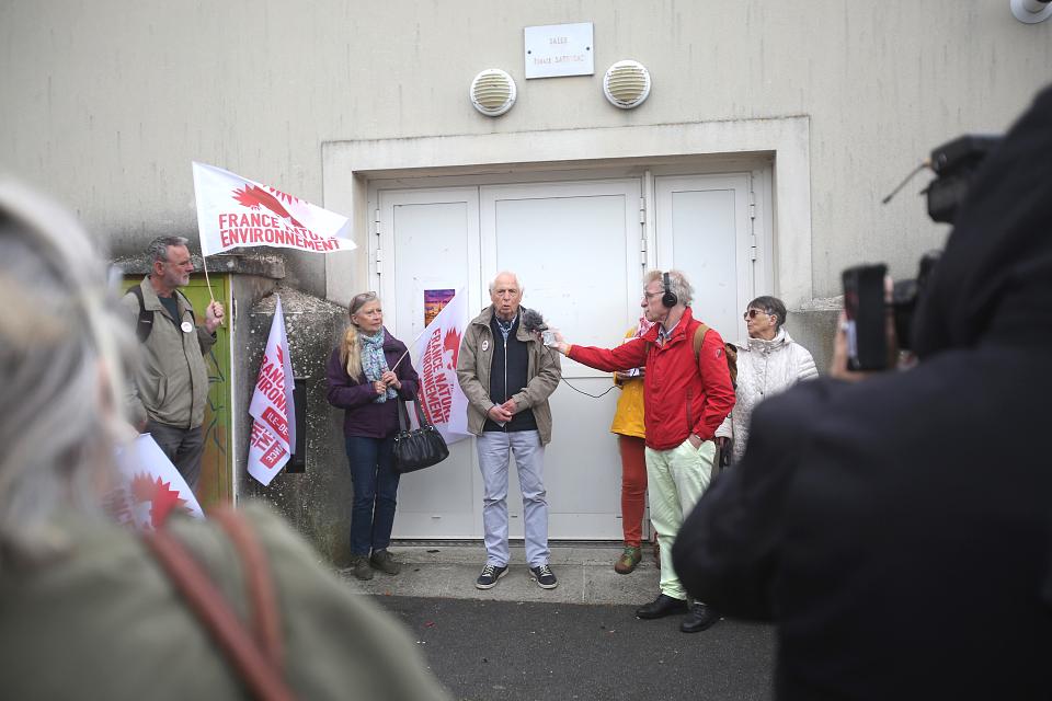 Un homme parle au milieu d'un rassemblement. Des personnes portent des drapeaux de France nature environnement.
