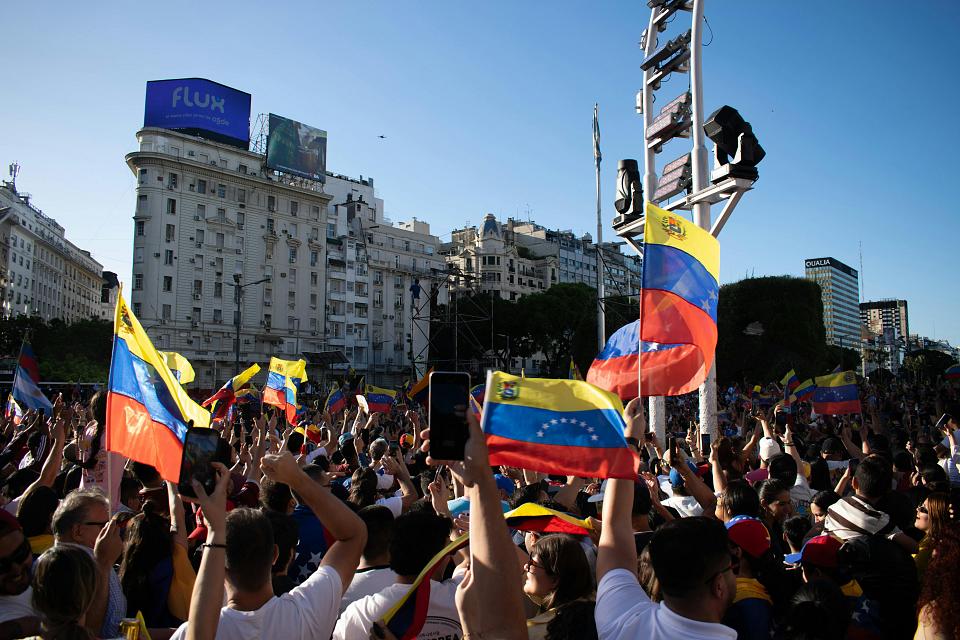 Un rassemblement sur une place, les personnes portent des drapeaux du Venezuela. 