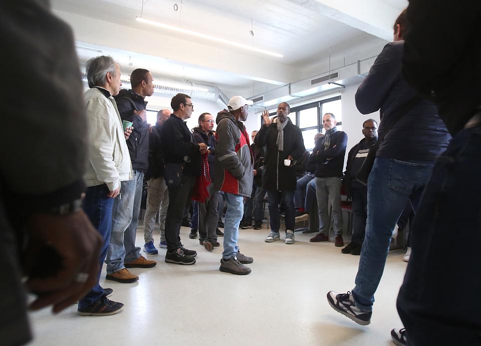Des hommes debout dans une salle, l'un d'entre eux parle.