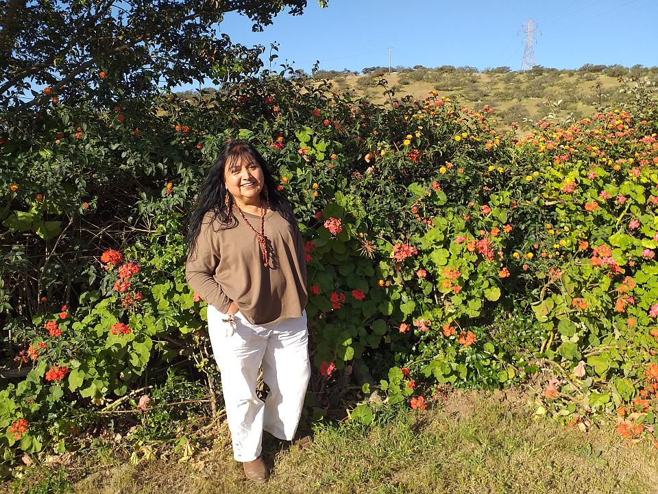 Une femme souriante devant une haie fleurie. 