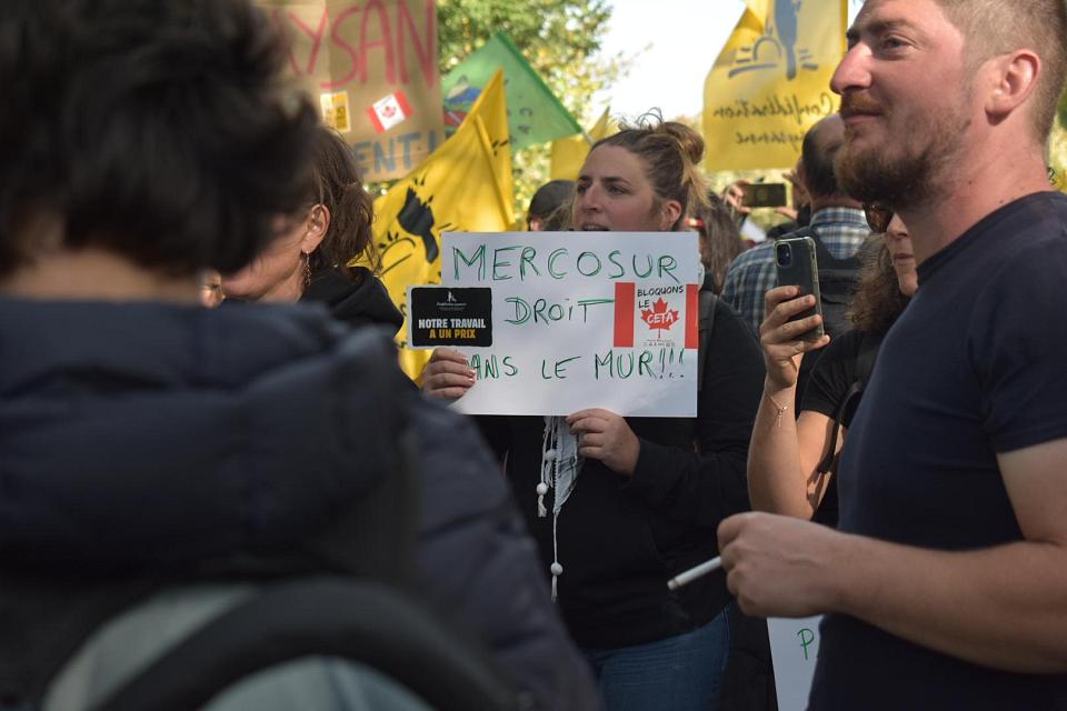 une femme porte une pancarte "Mercosur droit dans le mur" avec un autocollant "notre travail a un prix"