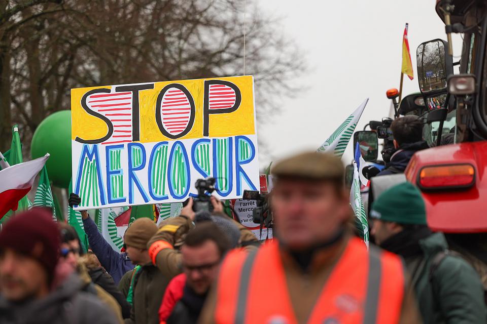 Des agriculteurs brandissent des pancartes, des drapeaux et des ballons. Sur une pancarte il est écrit « Stop Mercosur ». In distingue un tracteur. 