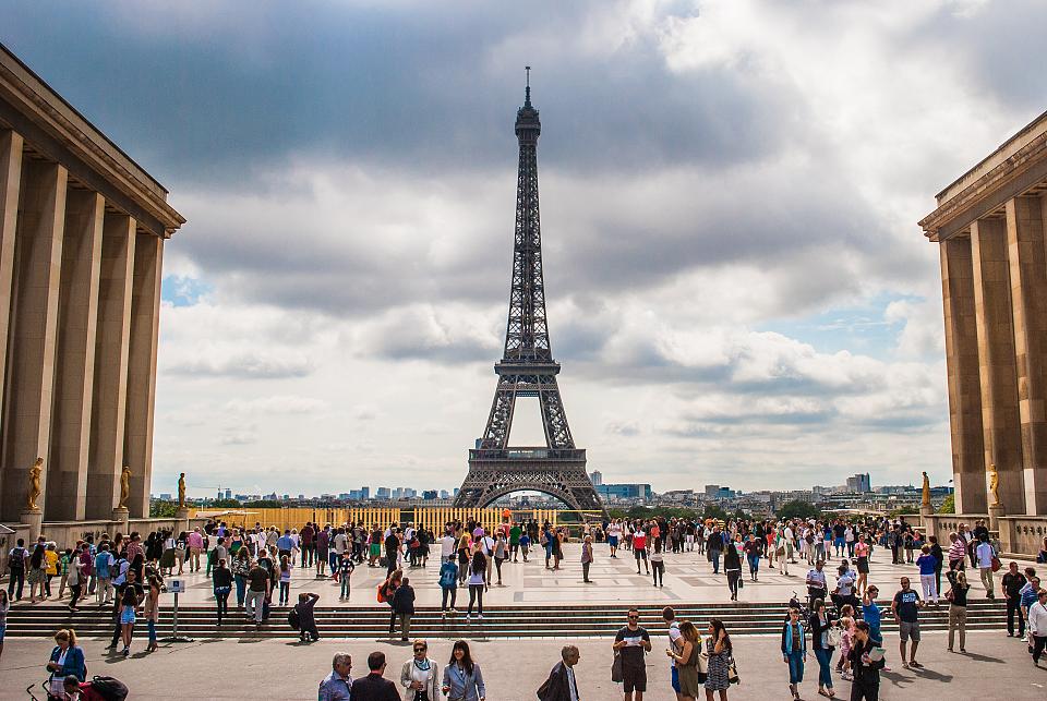 Vue du parvis devant la tour Eiifel, plein de monde qui déambule. 