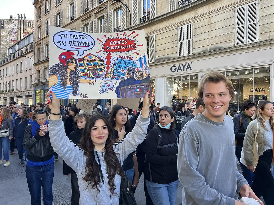 une jeune femme porte une pancarte "tu casses tu répares" en faisan référence aux coupes budgétaires
