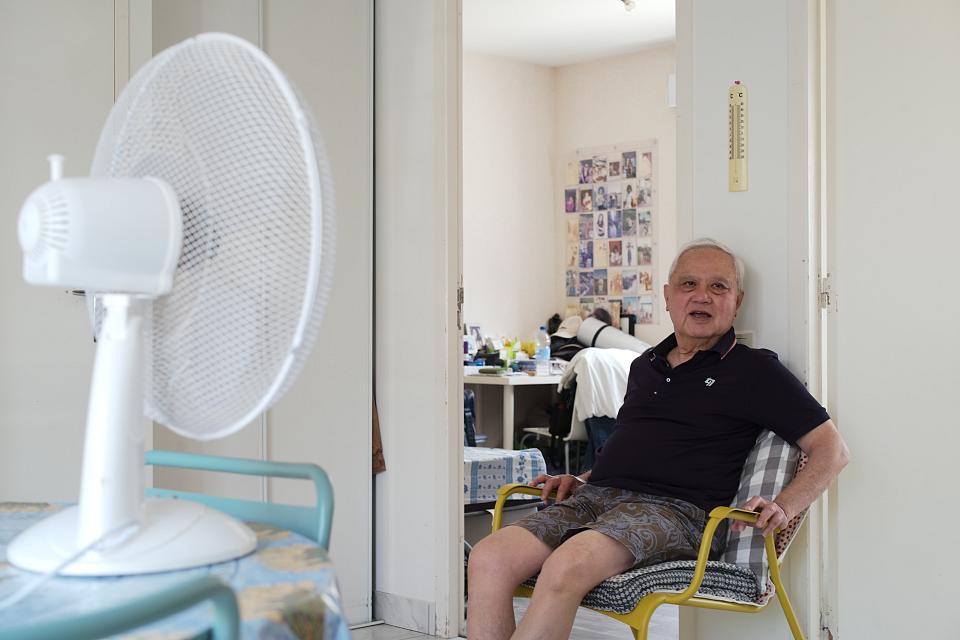 Un homme âgé est assis face à un ventilateur dans un logement.