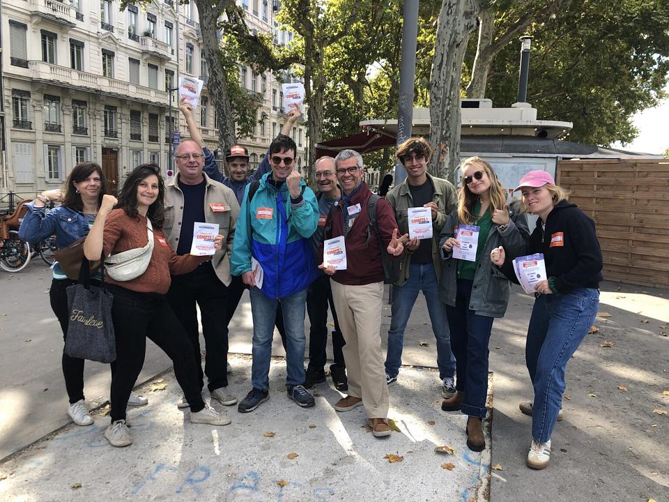 Un groupe de dix personnes souriantes pose en regardant vers l'objectif des tracts à la main. 