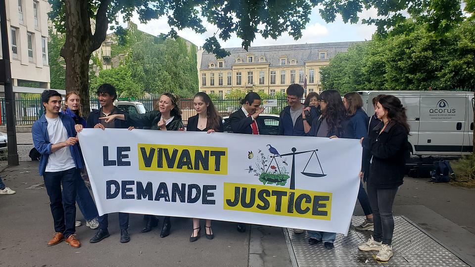 Des personnes debout tiennent une banderole sur laquelle il est écrit "Le Vivant demande justice".