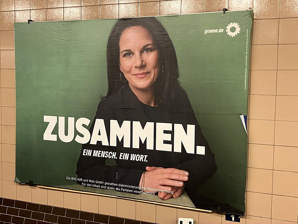 Annalena Baerbock, ministre verte des Affaires étrangères, souriante sur son fond sur une affiche de campagne dans un couloir de métro. Il est écrit en gros "Zusammen". 
