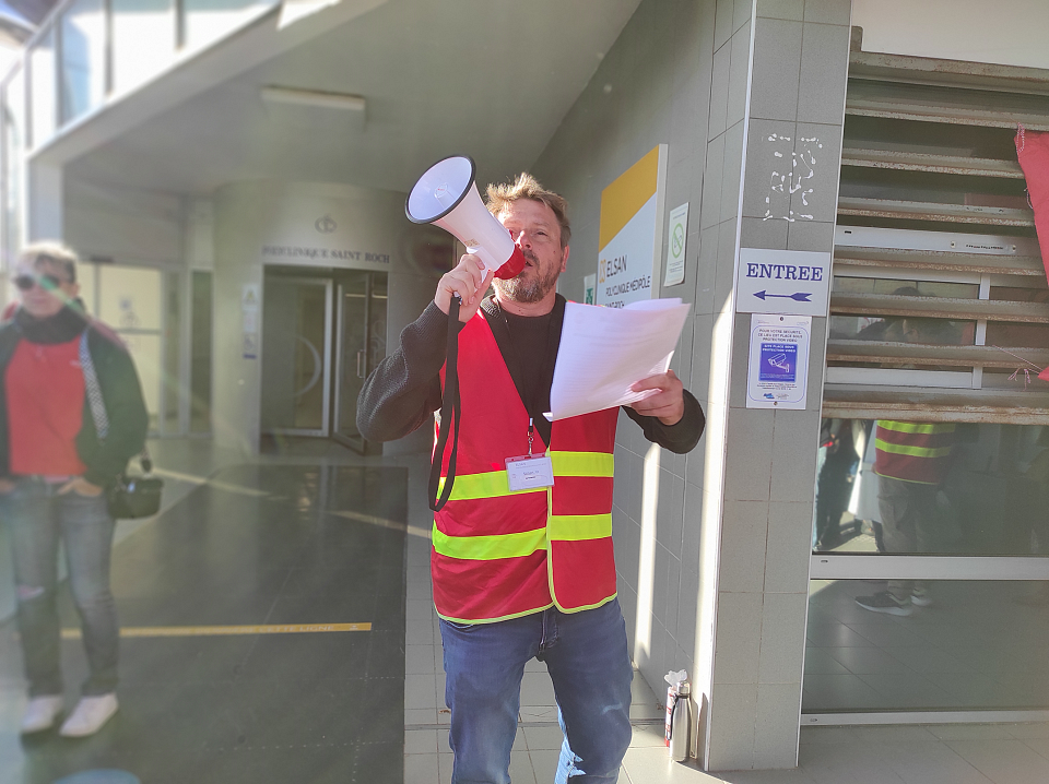 Un homme vêtu d'un gilet syndical parle dans un mégaphone.