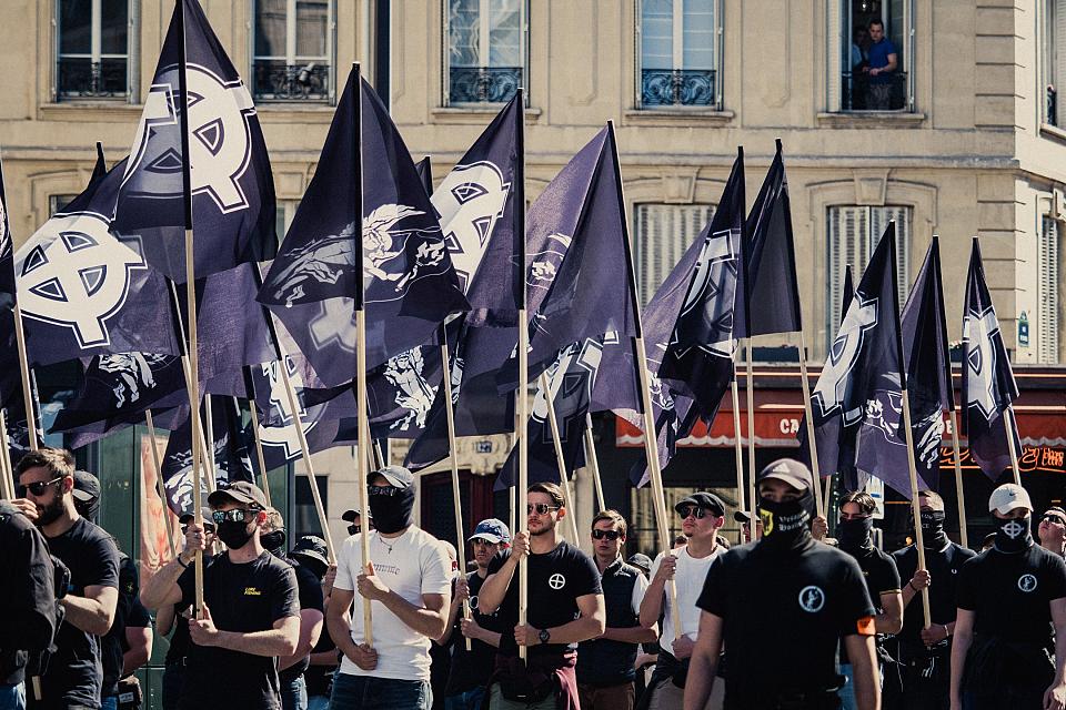 Plusieurs rangées de militants d'extrême droite portant des drapeaux arborant une croix celtique blanche sur fond noir