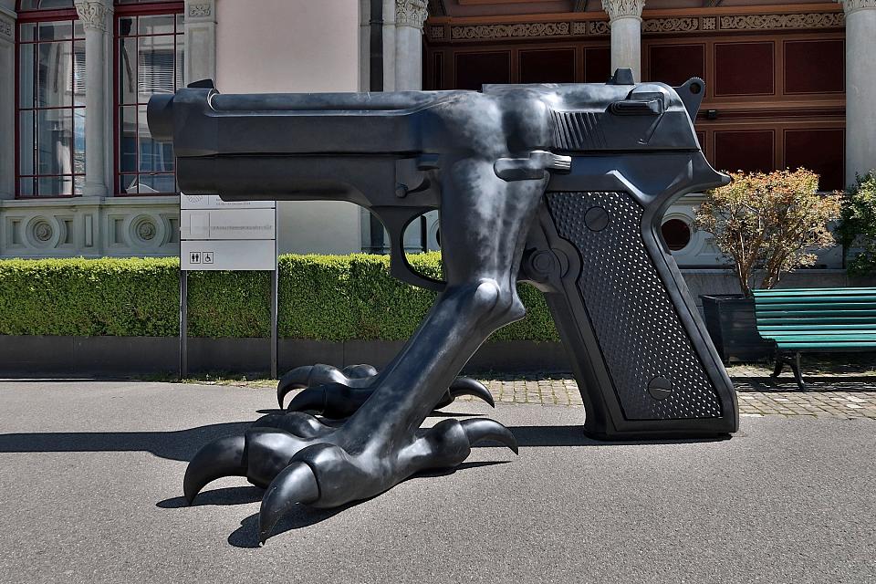 Une sculpture dans une rue représentant un immense pistolet muni de pattes monstrueuses. 