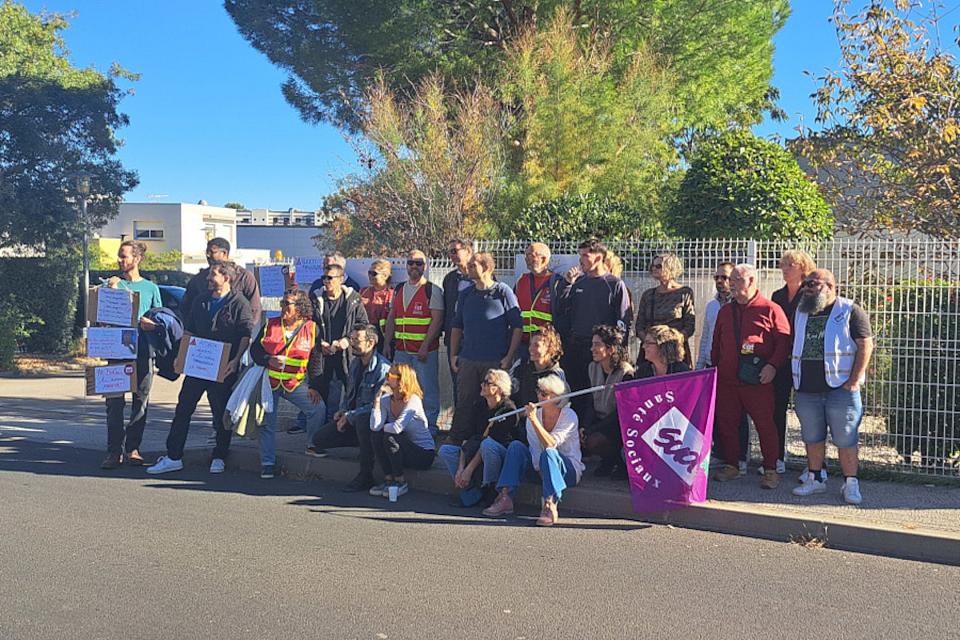 Des personnes rassemblée posent pour une photo avec des chasubles et des drapeaux de Sud Santé sociaux. 