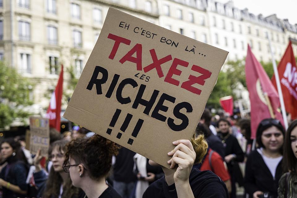 Un manifestant tient une pancarte avec le texte «Eh c'est bon là...Taxer les riches». 