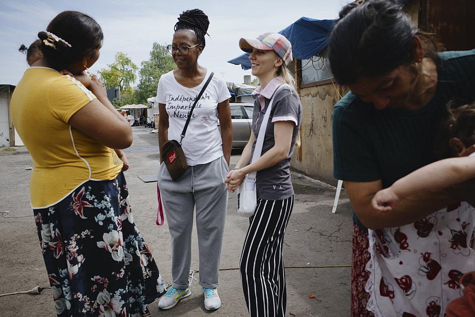 Deux femmes discutent debout avec une autre, qui porte un bébé. Une quatrième femme tient dans ses bras un autre enfant.