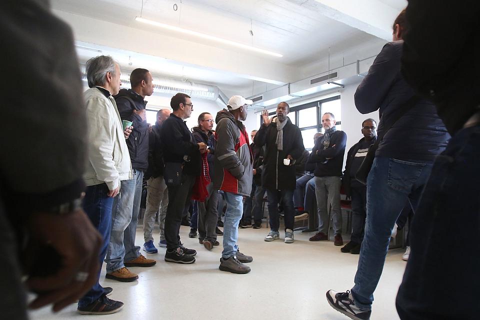 Des hommes debout dans une salle, l'un d'entre eux parle.