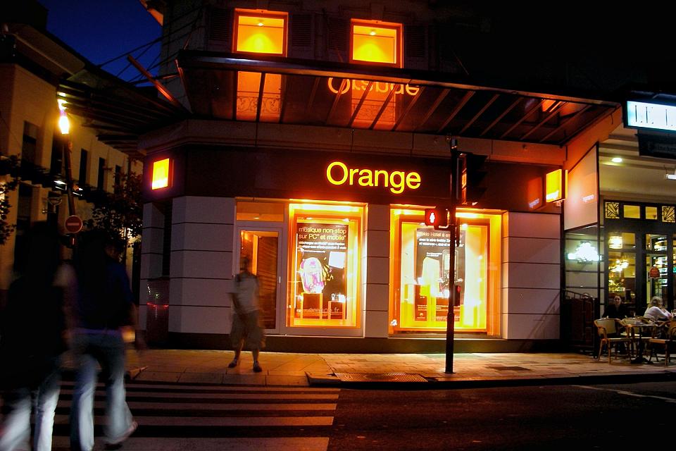 Une boutique Orange dans une ville la nuit, le nom “Orange” est illuminé en orange.