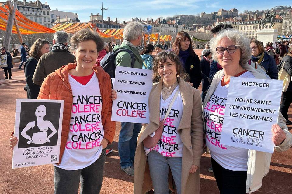 Des panneaux "Cancer colère" tenus par trois personnes