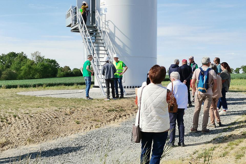 Des personnes font la queue au pied d'un mât d'éolienne.