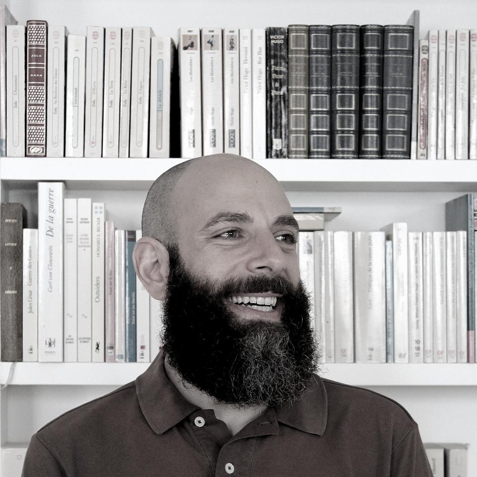 Photo en noir et blanc d'un homme souriant devant une bibliothèque