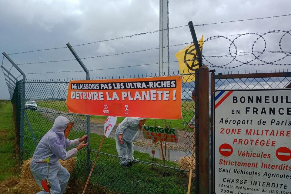 des militants en combinaison blanche pénètrent sur une zone aéroportuaire grillagée avec une banderole "ne laissons pas les ultra-riches détruire la planète"