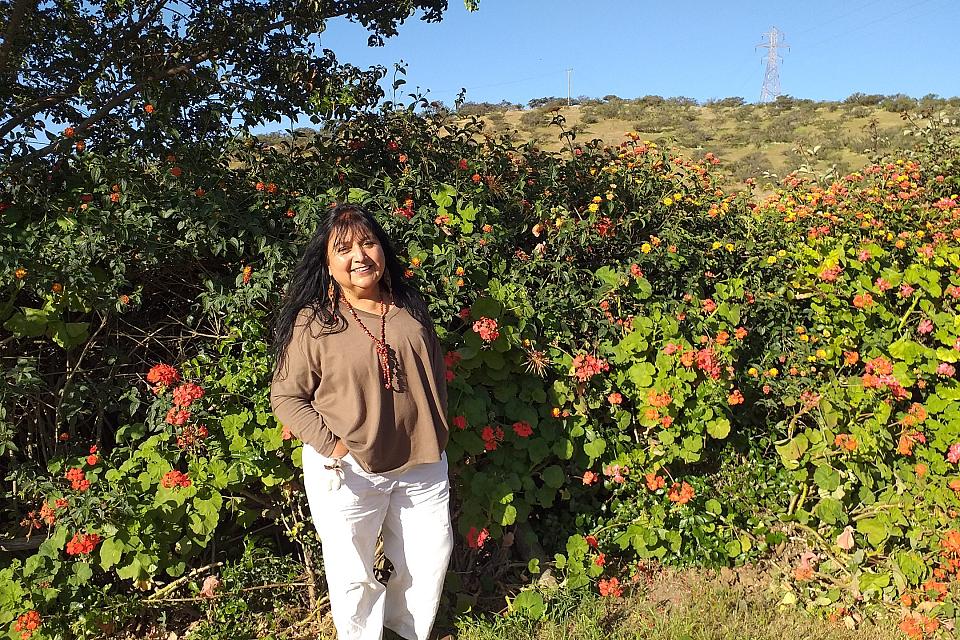 Une femme souriante devant une haie fleurie.