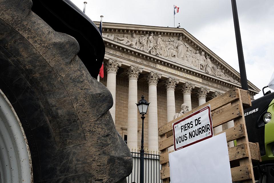 une roue de tracteur, un panneau "fiers de vous nourrir" et au fond la façade de l'assemblée nationale