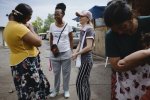 Deux femmes discutent debout avec une autre, qui porte un bébé. Une quatrième femme tient dans ses bras un autre enfant.