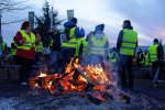 des personnes en gilets jaunes de dos devant un feu de palettes