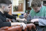 Tournevis et jauge de réglage à la main, deux étudiants en BTS en alternance s'entrainent au réglage des culbuteurs d'un moteur de camion dans un atelier.