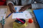 Des mains d'élève sur une table de classe en gros plan, l'élève trace une ligne sur une feuille à l'aide d'une règle.
