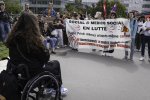 Des manifestantes et manifestants tiennent une banderole avec le texte «Social et médico-social en lutte. Public, Privé, mêmes attaques, même combat. Ni licenciements. Financement a hauteur des besoins, ni coupes budgétaires». Une personne en fauteuil roulant leur fait face.