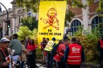 Des manifestants dont certains avec un chasuble rouge de la CGT devant une banderole jaune sur laquelle est dessinée en rouge un tête de mort coiffée d'un casque de chantier et est écrit « BTP, un mort par jour ». 