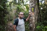 Un homme souriant montre une marque de pas inscrite sur un arbre. 