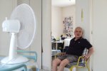 Un homme âgé est assis face à un ventilateur dans un logement.