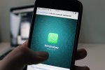 Une main tient un smartphone sur lequel se trouve l'application WhatsApp