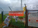 des militants en combinaison blanche pénètrent sur une zone aéroportuaire grillagée avec une banderole 