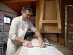 Un homme avec un tablier blanc façonne des pains au levain dans son fournil