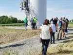 Des personnes font la queue au pied d'un mât d'éolienne. 