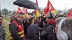 Une femme parle avec des hommes en chasubles rouge et avec des drapeaux de la CGT, un homme filme. 