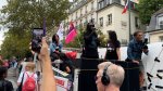 Plusieurs personnes sont à l'arrière d'un camion. A l'avant un homme parle dans un micro. Au premier plan, une personne filme avec son téléphone.