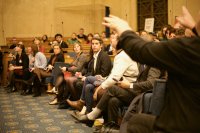 Gabriel Attal assis sur les bancs en bois d'une salle au milieu d'une vingatine d'autres personnes. 