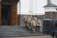 Six hommes en uniforme, vus de dos, portent à cercueil, d'une voiture à un bâtiment dont les portes sont ouvertes.