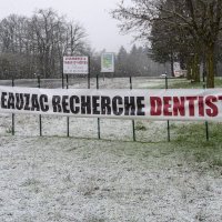 Une banderole sur laquelle il est écrit "Beauzac recherche dentiste" au bord d'une route dans un décor enneigé. 