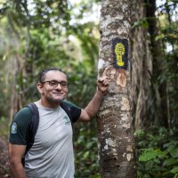 Un homme souriant montre une marque de pas inscrite sur un arbre. 